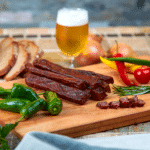 Landjäger -Bregenzerwälder Landjäger auf einem Frühstücksbrett mit Bier im Hintergrund
