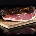 Traditionell hergestellter Schinkenspeck aus Österreich im Anschnitt, auf Holzbrett angerichtet – naturbelassen, ohne unnötige Zusatzstoffe, im Almgold-Onlineshop erhältlich
