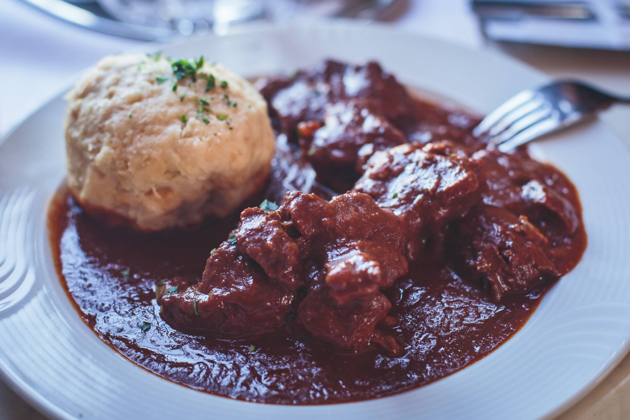 saftiger Rindergulsch mit Semmelknödel auf einem weißen Teller serviert