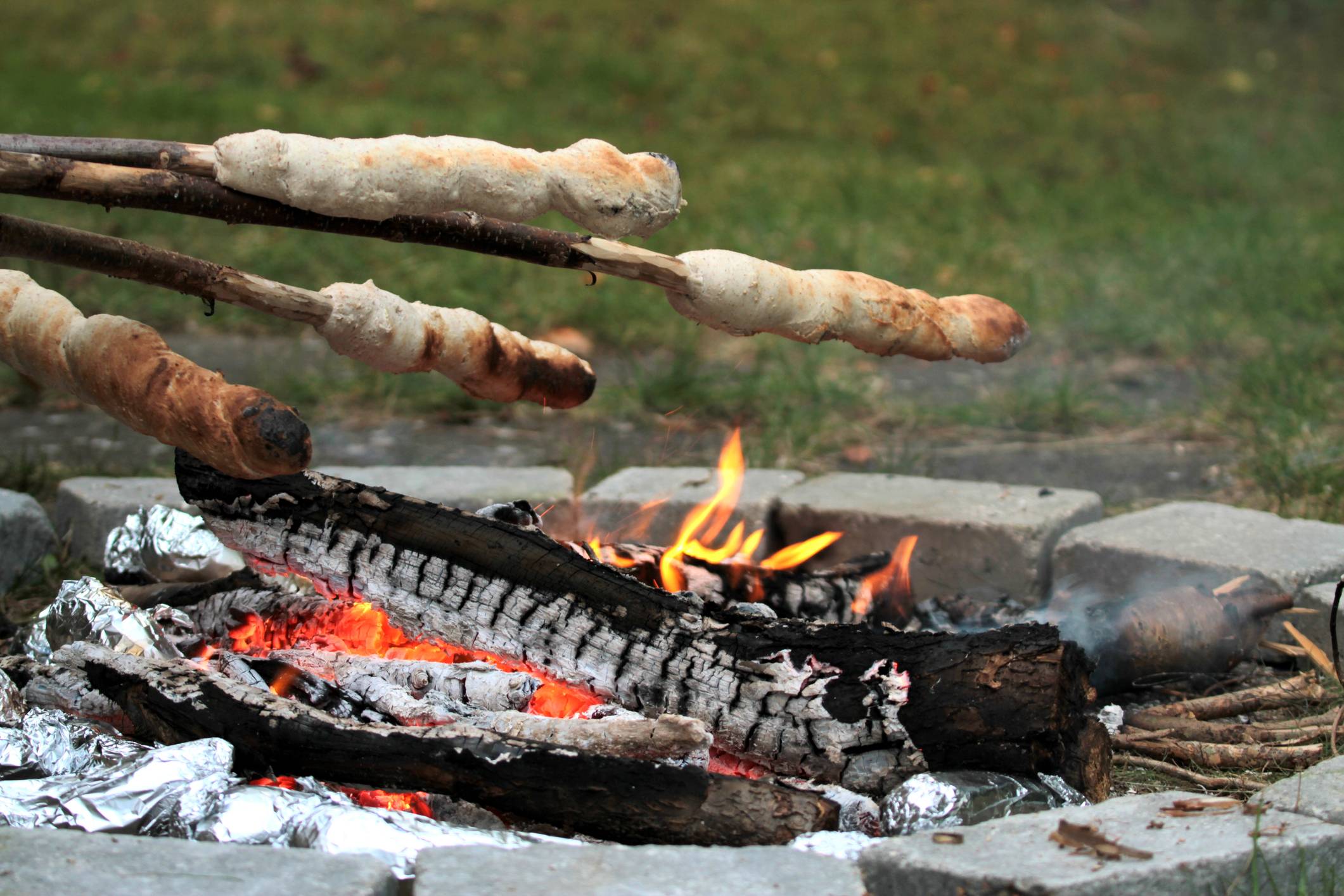 mehrere Stück Stockbrot werden ins Lagerfeuer gehalten