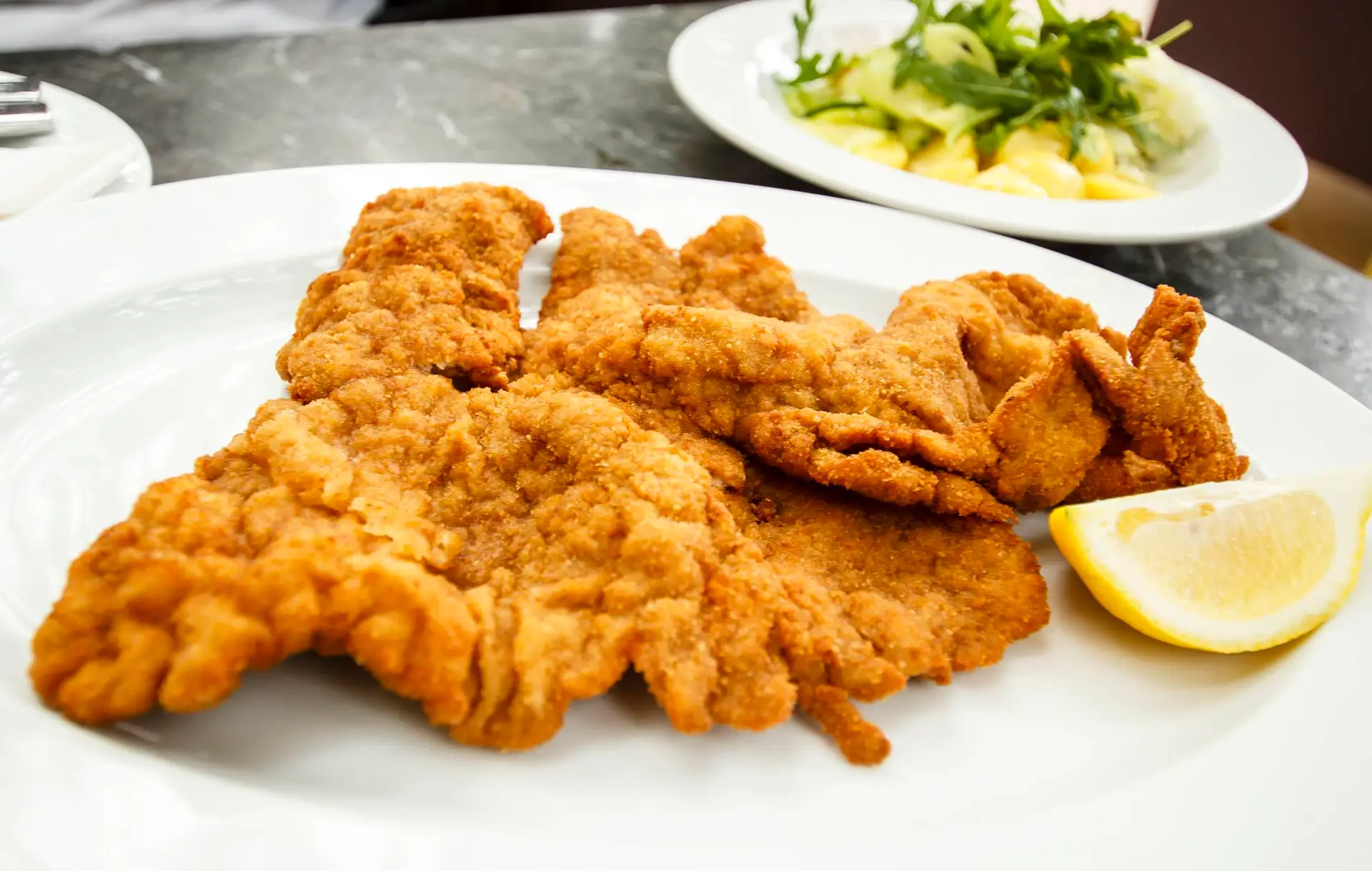 Original Wiener Schnitzel mit Kartoffelsalat und Zitrone auf weißem Teller serviert